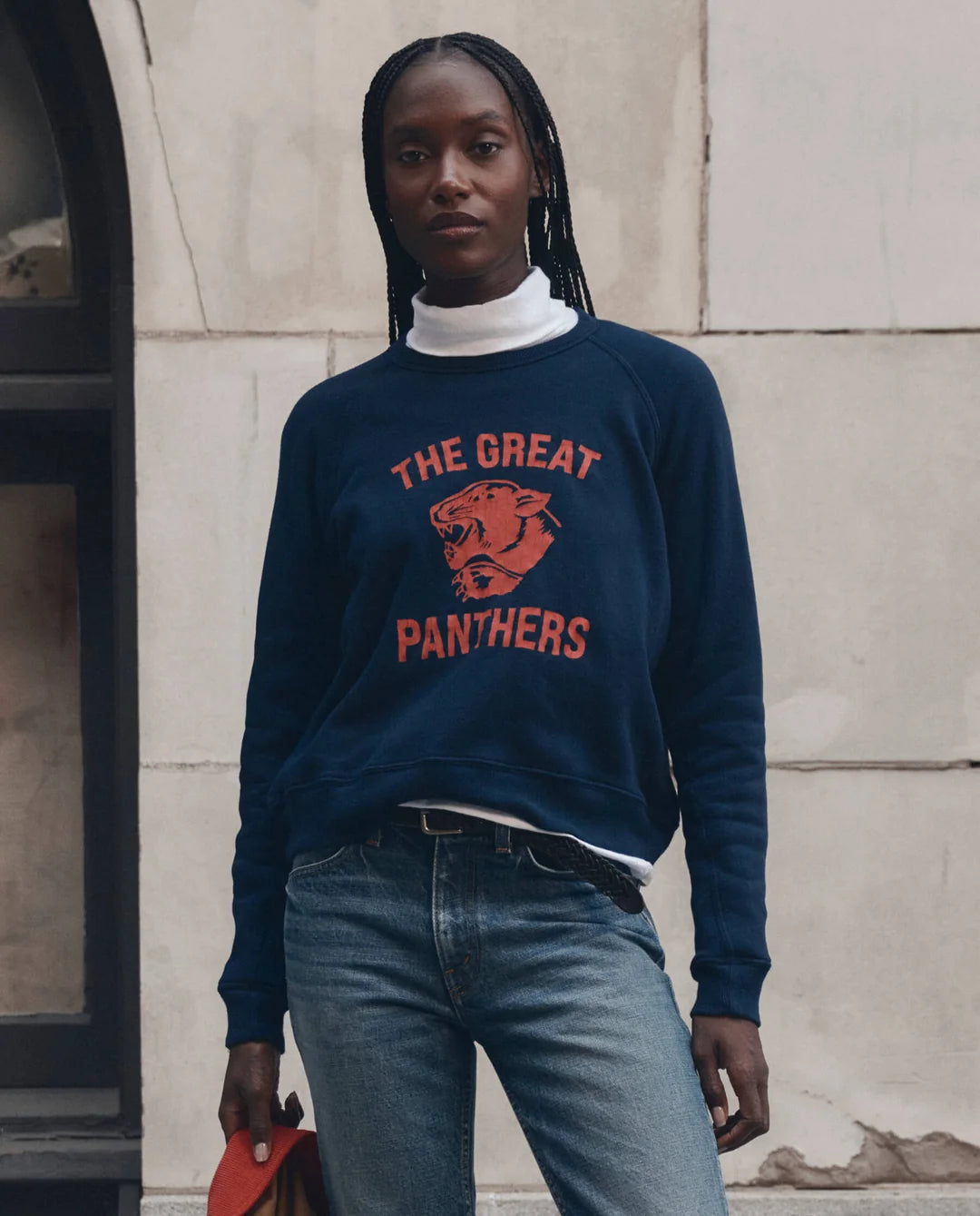 The Great Inc. Fleece Rookie Growling Panther sweatshirt styled casually with jeans by a stone wall.
