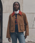 The Great Inc. Swingy Jacket in white with turtleneck, blue jeans, styled by a light stone wall for a casual look.