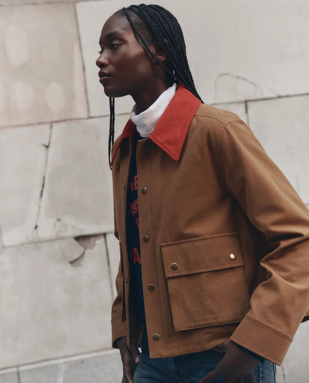 Swingy jacket with red collar by The Great Inc., styled with braids beside a textured stone wall.