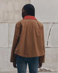 The Great Inc. Swingy Jacket in a casual style, shown with blue jeans against a cracked wall backdrop.