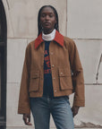 The Great Inc. Swingy Jacket in white with turtleneck, blue jeans, styled by a light stone wall for a casual look.