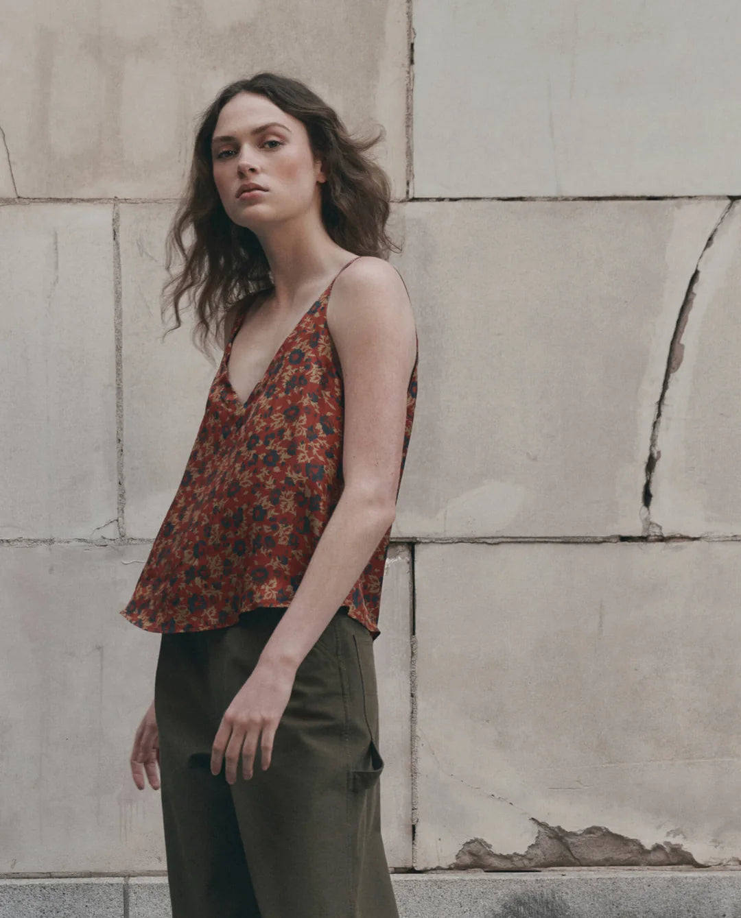 The Great Inc. Port Cami in green, styled with matching pants against a rustic stone wall backdrop.