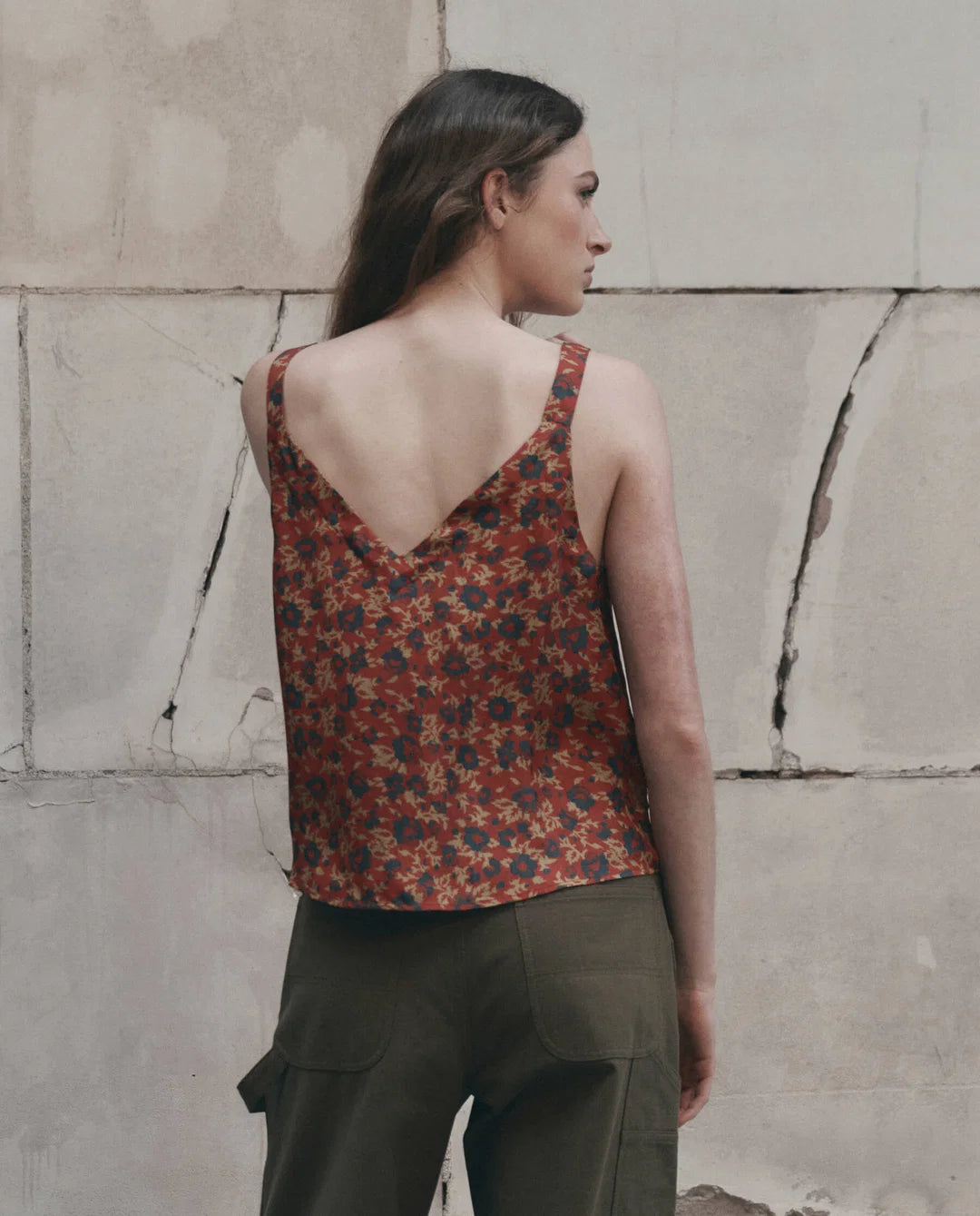 The Port Cami by The Great Inc. in off-white, styled with green pants against a textured wall for a relaxed look.