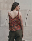 The Port Cami by The Great Inc. in off-white, styled with green pants against a textured wall for a relaxed look.