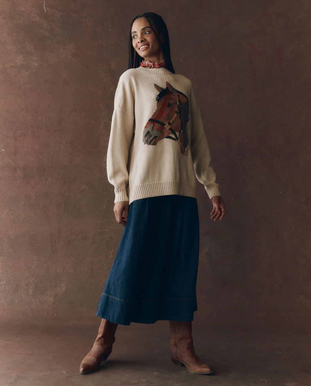 A woman wears The Great Inc. Stable Pullover, an oversized crew sweater, paired with a skirt.