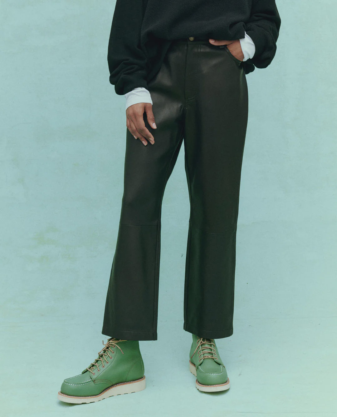 A person wearing &quot;The Leather Wayne&quot; slouchy leather pants from The Great Inc. stands against a light green background, with only the lower half of their body visible.