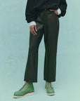 A person wearing "The Leather Wayne" slouchy leather pants from The Great Inc. stands against a light green background, with only the lower half of their body visible.