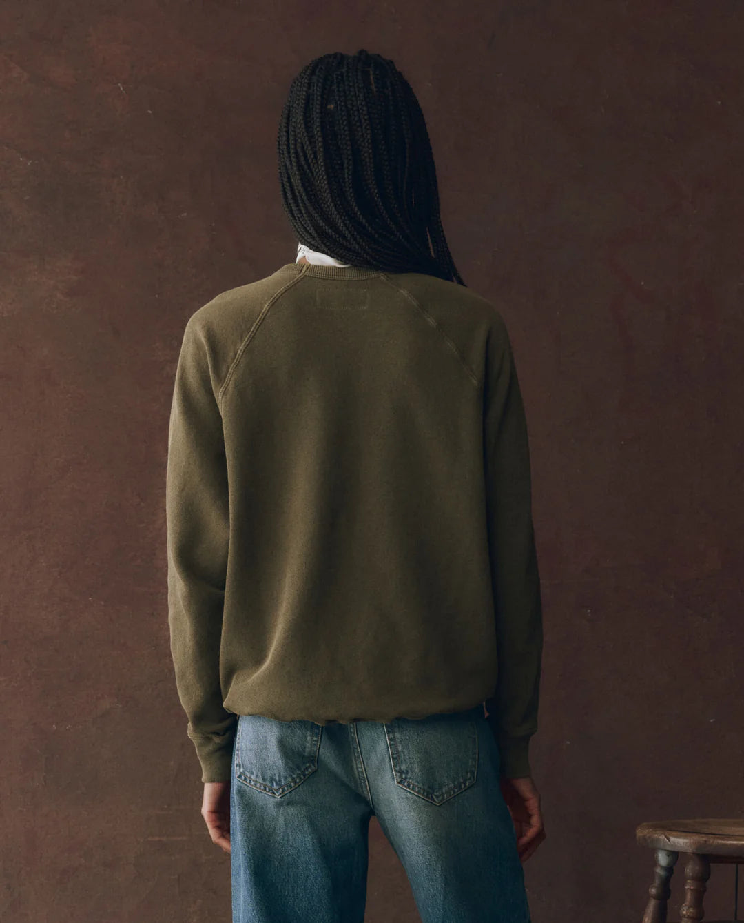 A person with braids wears The College Sweatshirt by The Great Inc., a green vintage style featuring a Wild Panther graphic.