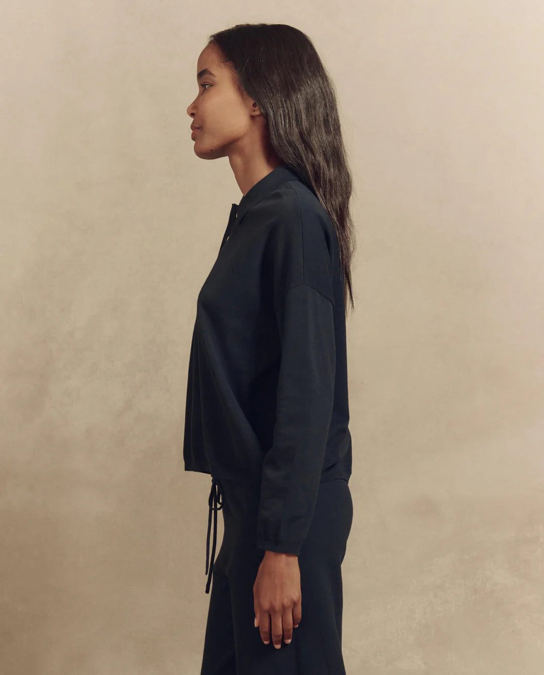 A person with long hair is shown in profile against a neutral backdrop, wearing The Great Inc.'s The Polo Sweater and matching pants.