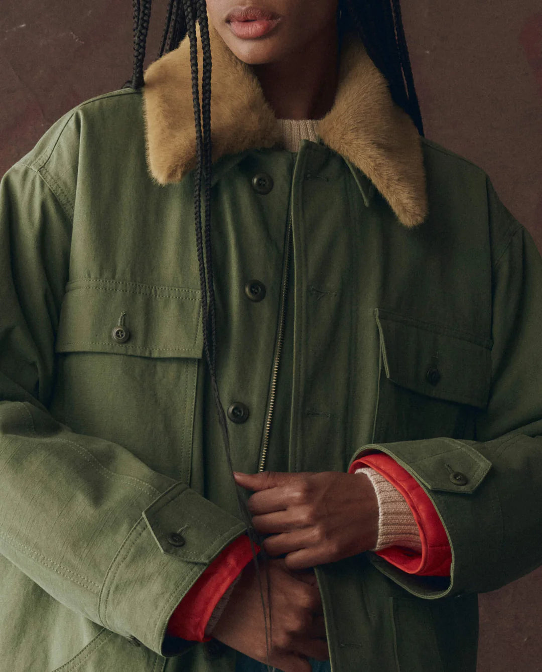 A person with dreadlocks wears The Quilted Liner Parka by The Great Inc., a green vintage-inspired military jacket with a removable faux fur collar.