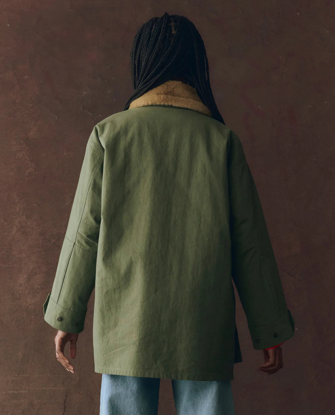 A person wearing The Great Inc.'s Quilted Liner Parka, a green parka featuring a quilted design and a removable faux fur collar.