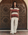 A woman stands before an ornate wooden door in The Boxy Crew 26 by The Great Inc., paired with cream wide-leg pants and brown shoes—effortlessly channeling a handcrafted Los Angeles aesthetic.