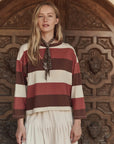 The Great Inc. Field Tee in striped pattern, styled with a bandana scarf, by an ornate wooden doorway.