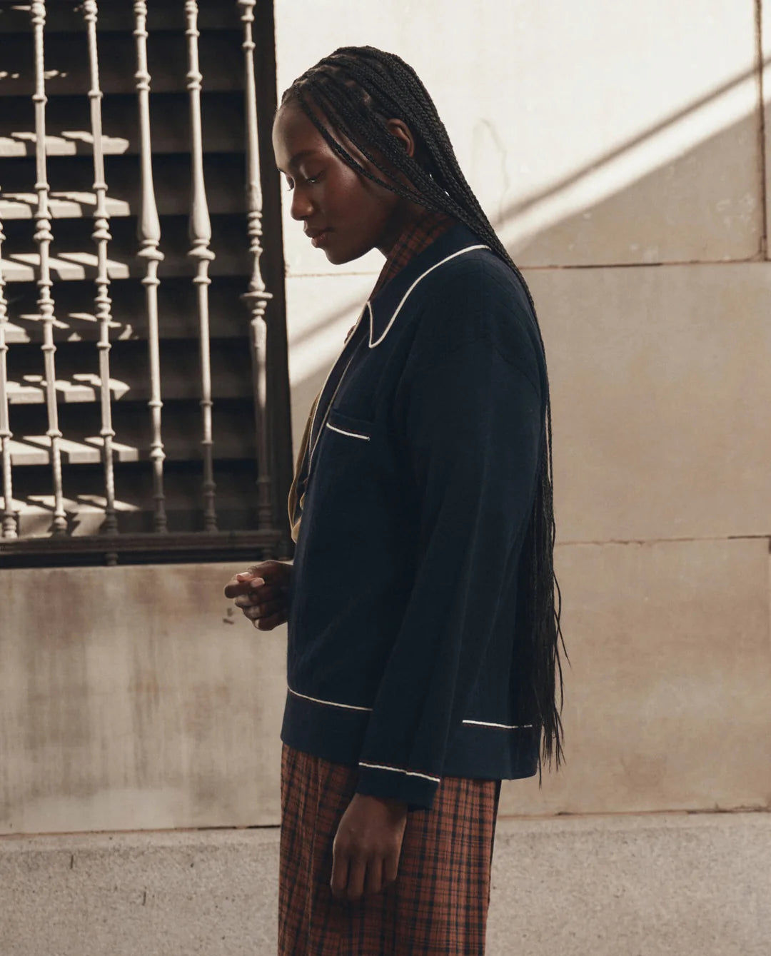 The Great Inc. menswear-inspired tipping polo and plaid skirt in natural light by a window with metal bars.