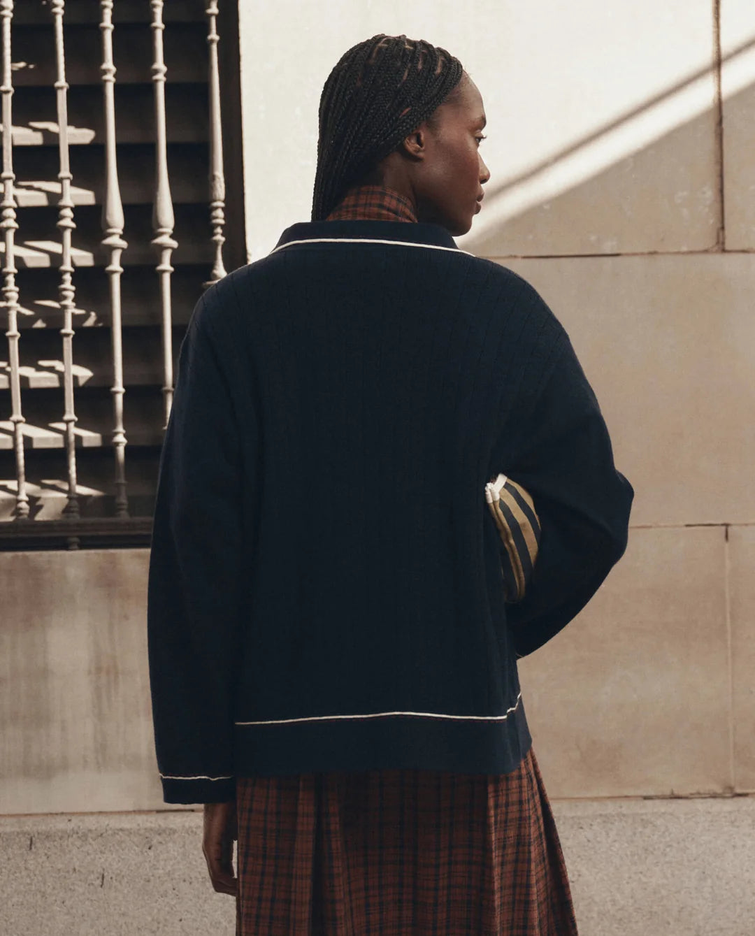 The Menswear Tipping Polo by The Great Inc., styled with a plaid dress and dark jacket, modern and chic look.