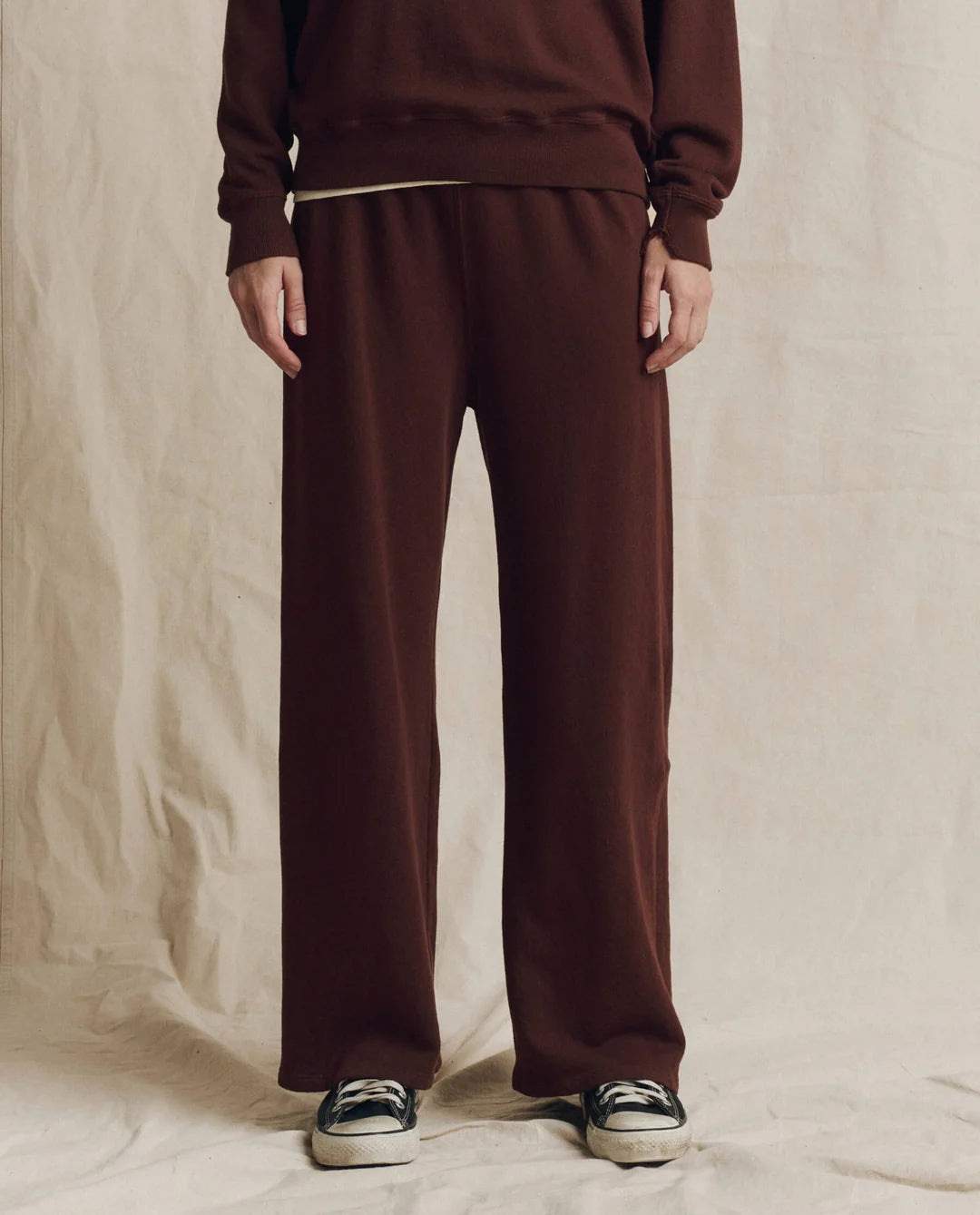 The Great Inc. Lap Sweatpant in brown, styled with a matching sweatshirt and sneakers on a beige background.