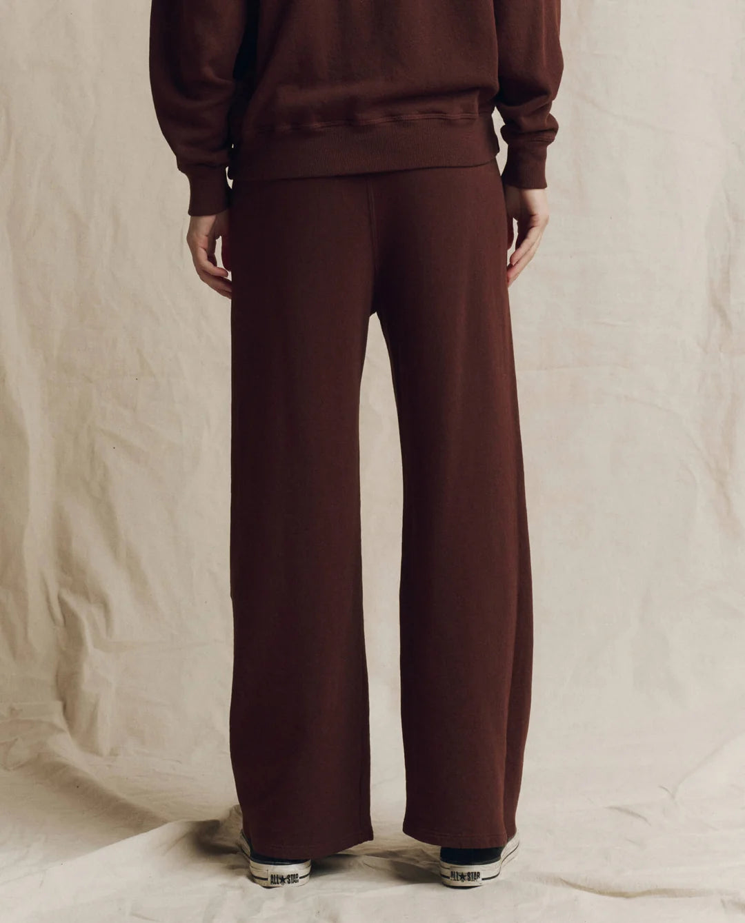 The Great Inc. brown wide-leg Lap Sweatpant with matching top, shown from the back on a cream fabric backdrop.