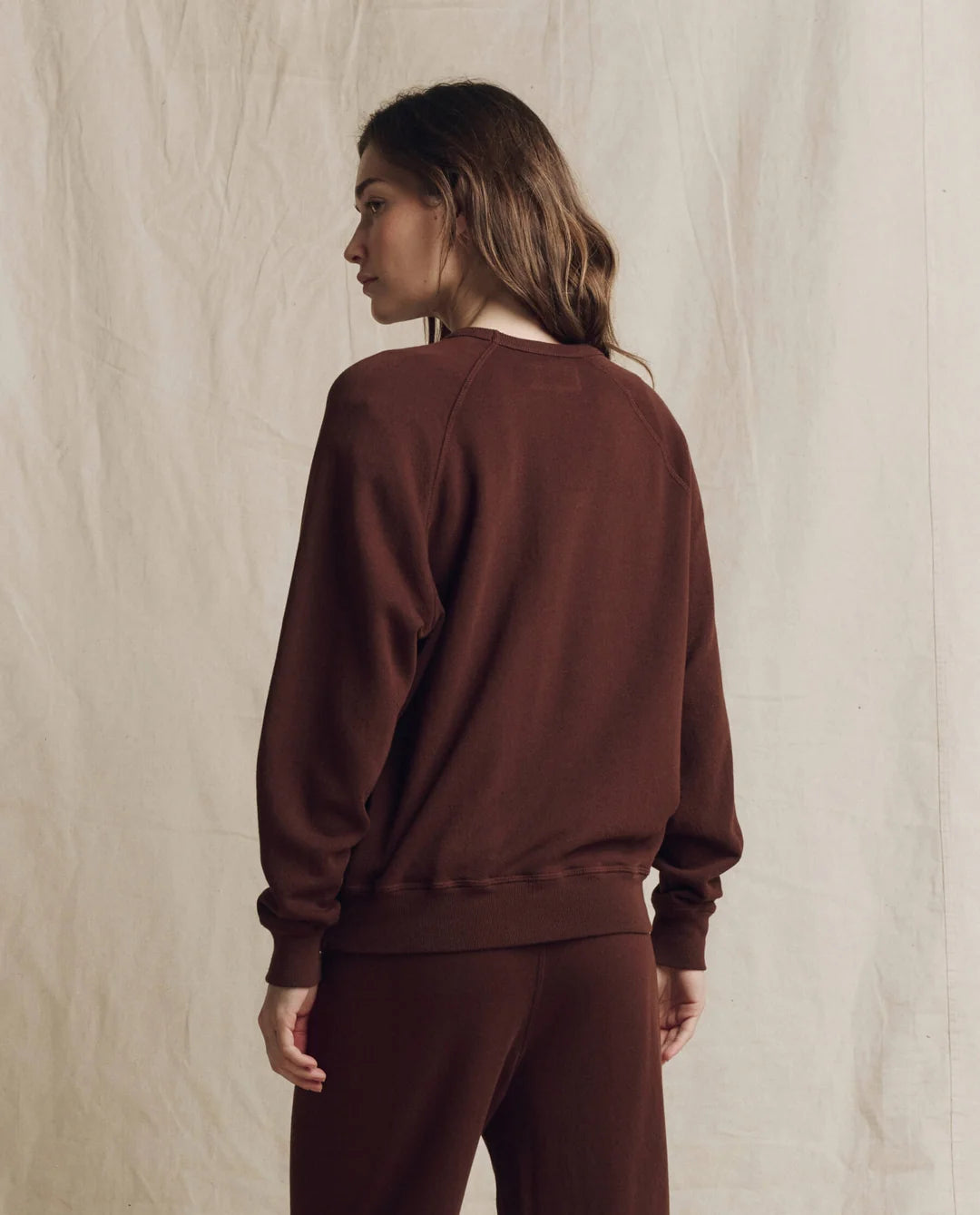 The Great Inc. College Sweatshirt 2026 in beige, modeled by a woman with long brown hair against a neutral backdrop.