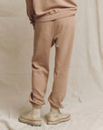 A person wearing The Stadium Sweatpant by The Great Inc. along with high-top off-white sneakers, reminiscent of vintage athletic wear, stands on a neutral fabric backdrop.