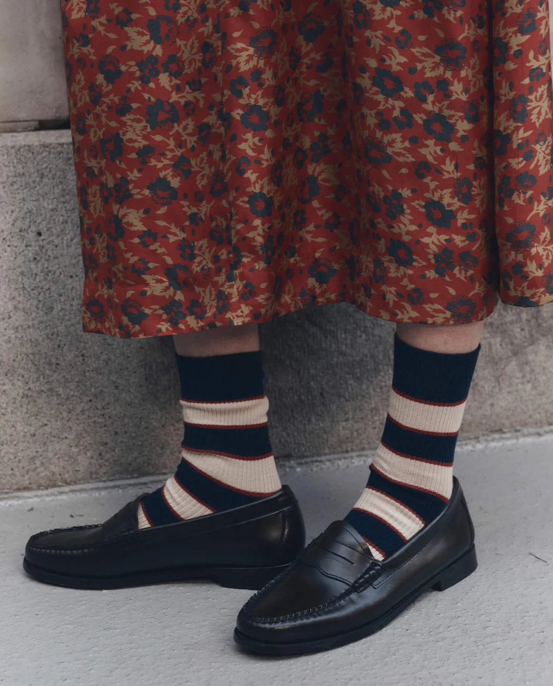 The Great Inc. Collegiate Sock in black, styled with a floral skirt and loafers on a light background.