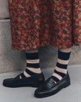 The Great Inc. Collegiate Sock in black, styled with a floral skirt and loafers on a light background.