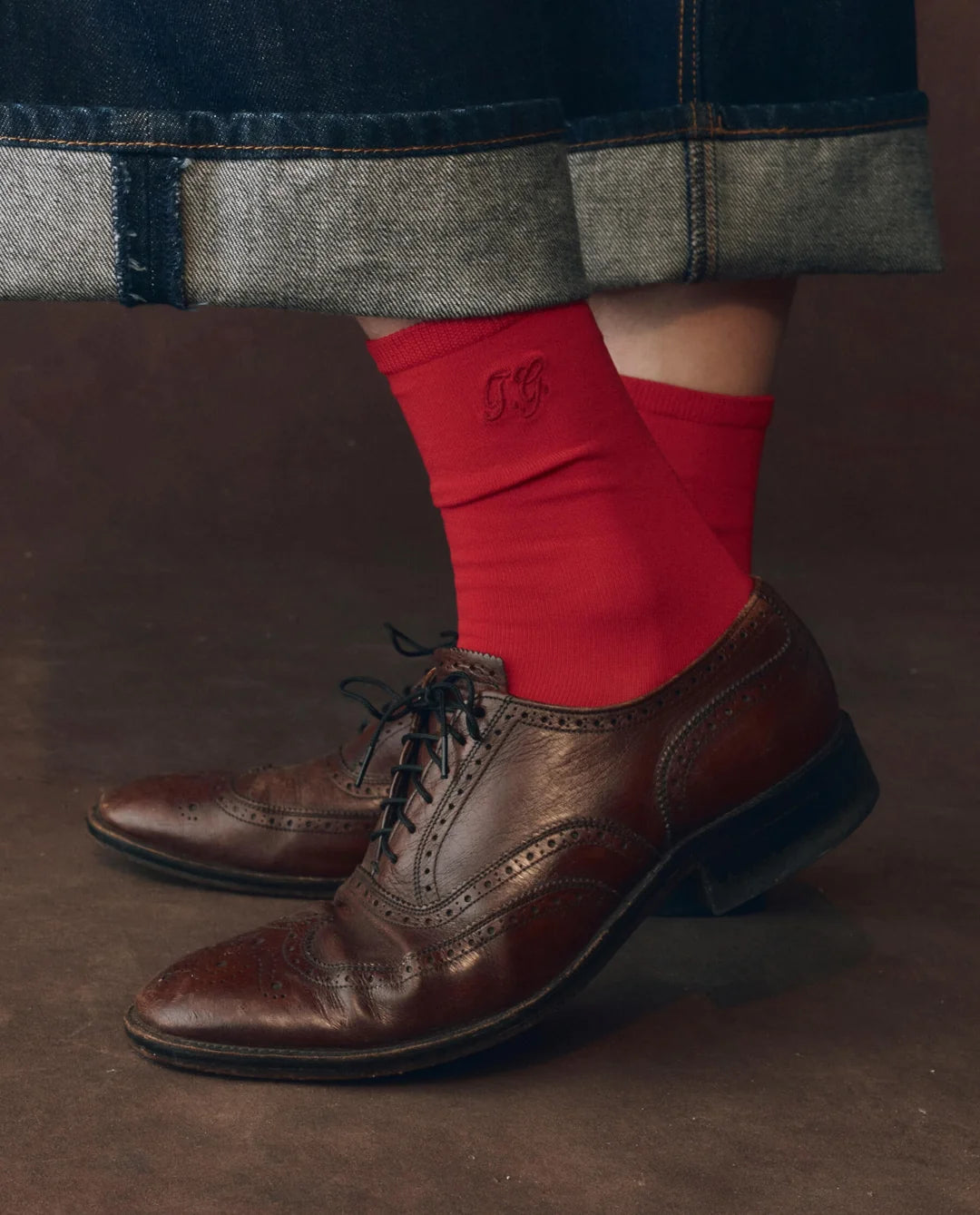 Bright red cotton The Great Inc. Monogrammed Trouser Socks styled with brown dress shoes and cuffed jeans.