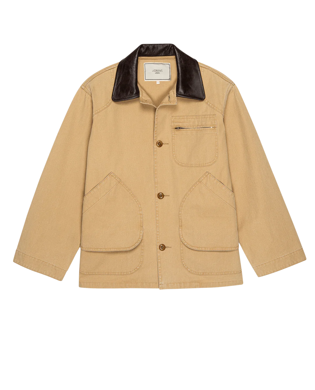 The Great Inc.'s Barn Jacket is a tan, garment-dyed cotton workwear jacket with brown buttons, utility pockets including a zip chest pocket, a dark brown leather collar, and an inner label for a casual yet structured look.