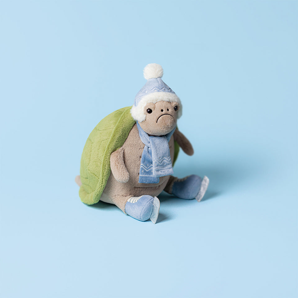 Timmy Turtle Skating by Jelly Cat Inc. is a festive plush turtle with a green shell, blue winter hat, scarf, and boots, ready for icy fun. He sits cheerfully on a light blue background.
