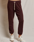 A person wearing the Toni French Terry Jogger by Perfectwhitetee in maroon and white sneakers with subtle brown accents stands against a plain beige background. The joggers feature an adjustable drawstring, and only the lower half of the body is visible.