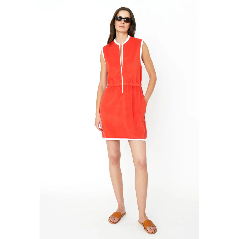 A person in The Terry Dress by Kule, featuring a sleeveless design with white trim and front zipper closure, stands against a white background wearing sunglasses and brown sandals.