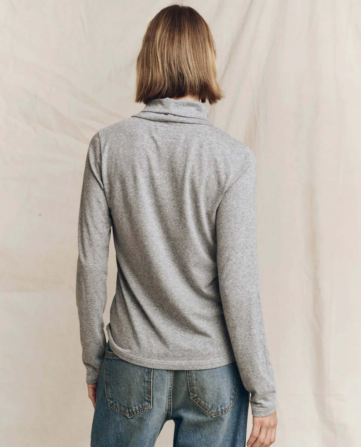 Grey heather turtleneck sweater from The Great Inc. paired with blue jeans, back view.