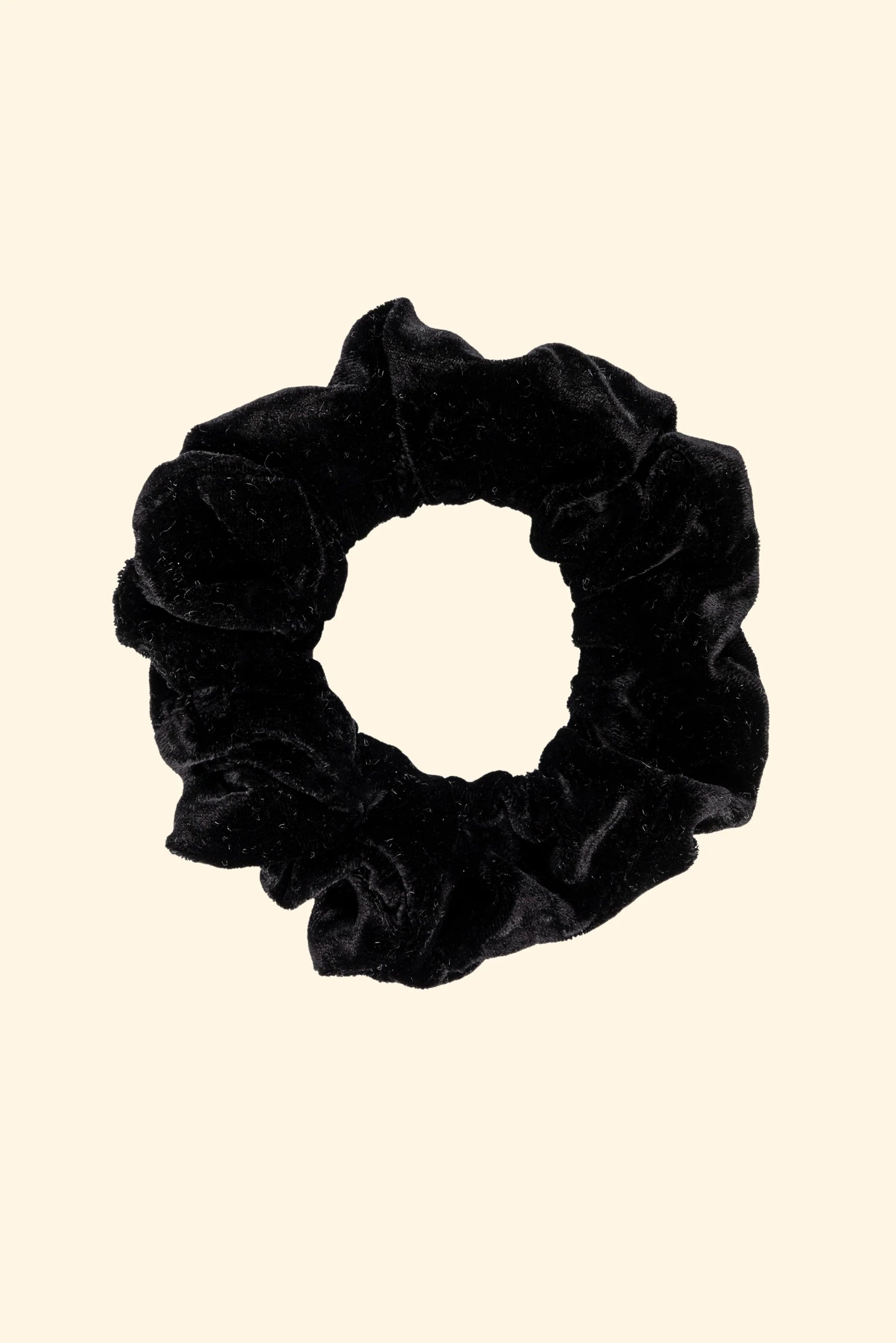 The Donni Velvet Scrunchie, a chic hair accessory, is showcased on a beige backdrop. Crafted in Los Angeles, the scrunchie features gathered black velvet for a textured, plush look.