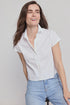 A woman with long brown hair wears THE SHIRT’s Boxy Short Sleeve Cropped Shirt in white and light blue jeans, smiling as she leans to the side against a plain light background.