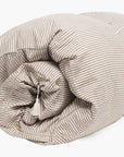 The Hedgehouse Throwbed is a rolled-up comforter in beige and white stripes, featuring a soft cushioned texture and a machine-washable cover, shown on a white background.