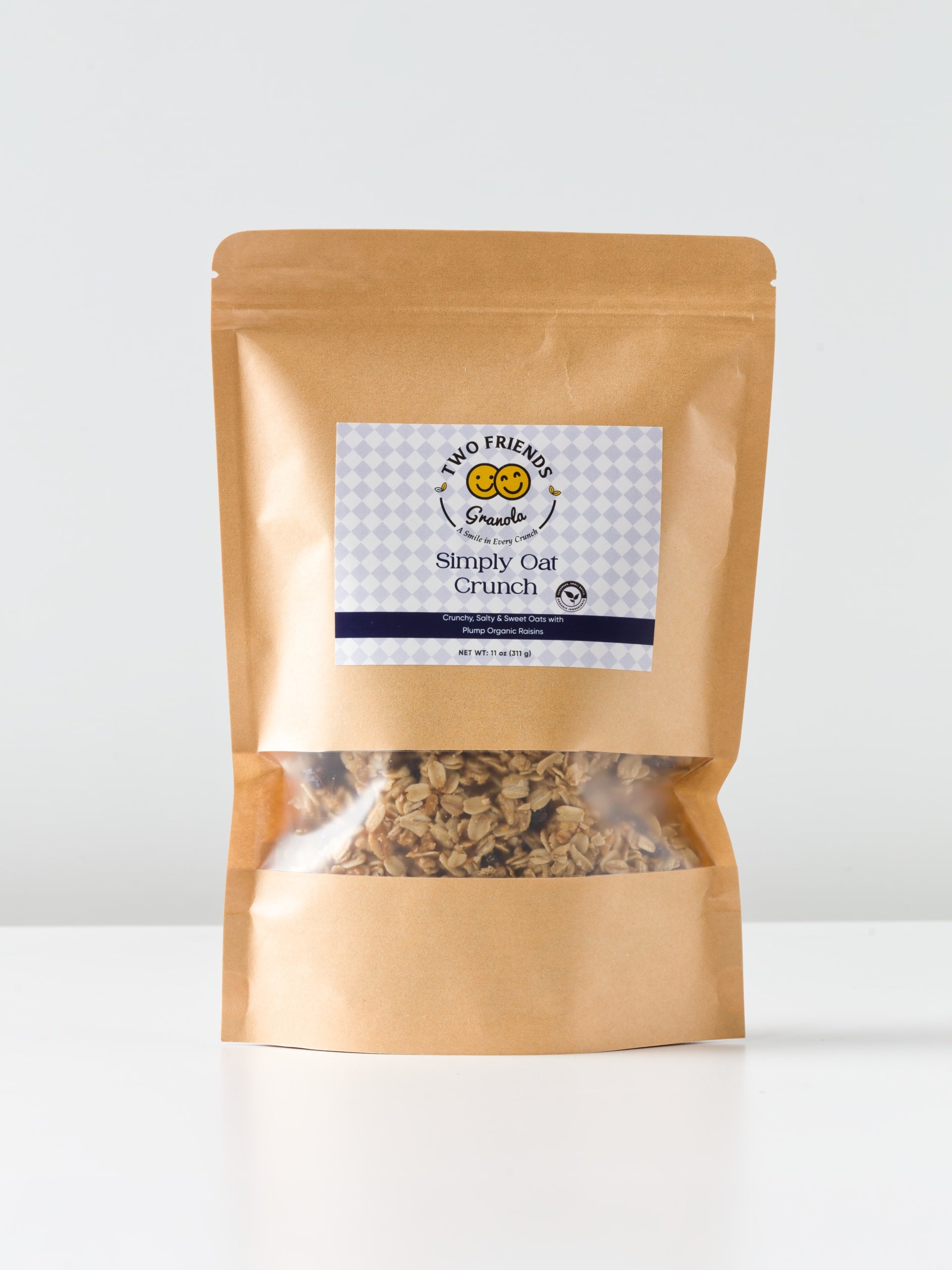 A brown, resealable pouch of Two Friends Granola's Simply Oat Crunch sits on a white surface, featuring a clear window showing oats and toasted coconut, and a label with a smiling sun logo.