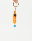 A hand holds The Upside's LIMITLESS KEYRING, a gold keyring with an orange macrame paracord keychain, blue-tipped ends, and a small metal star, shown against a plain white background.
