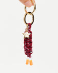 A hand displays The Upside LIMITLESS KEYRING, featuring maroon and white macrame paracord with orange-tipped ends and a gold star-shaped charm engraved with text.