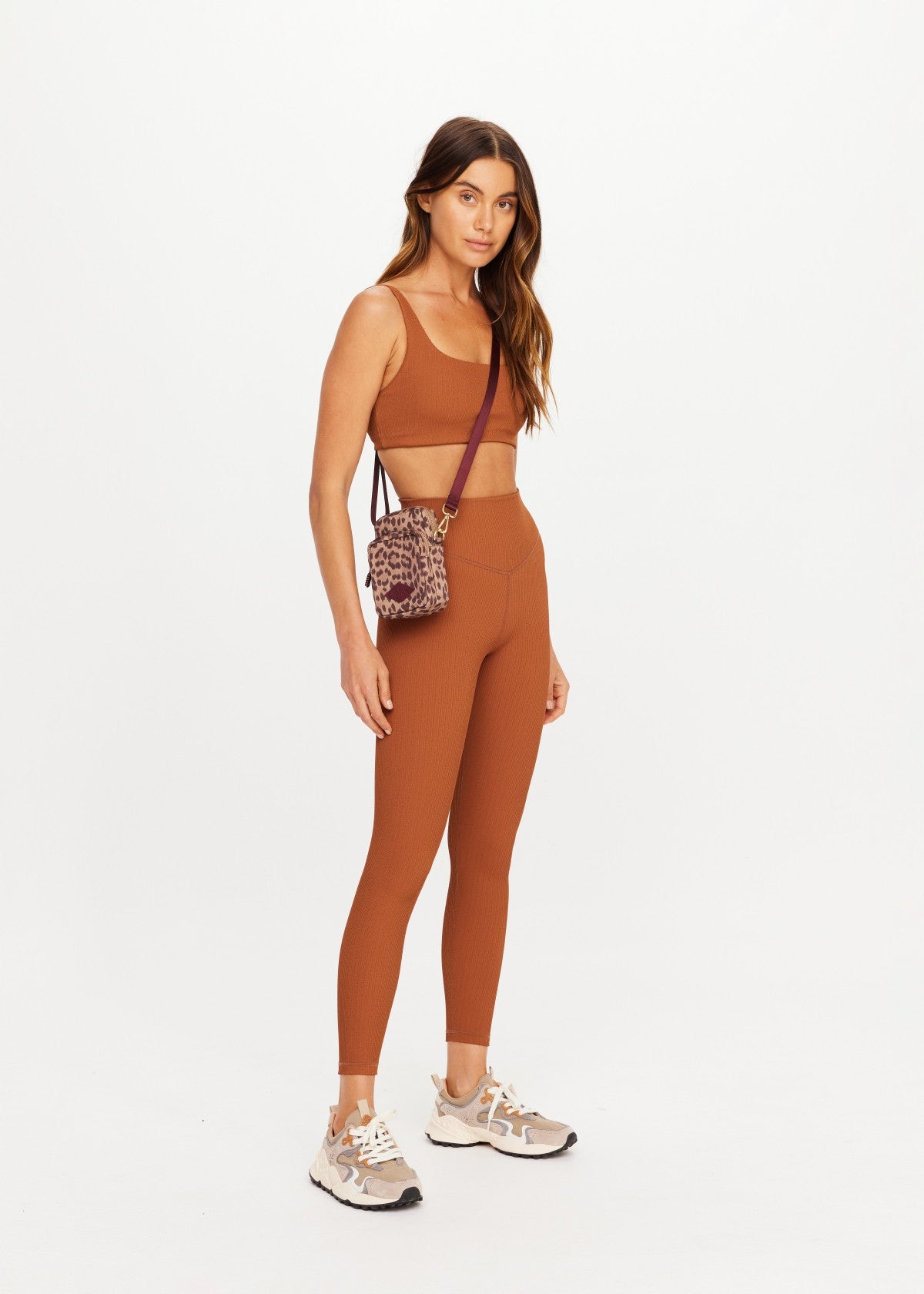 The Upside JAVAN LILO rust crossbody bag styled with athleisure outfit, shown on white background.