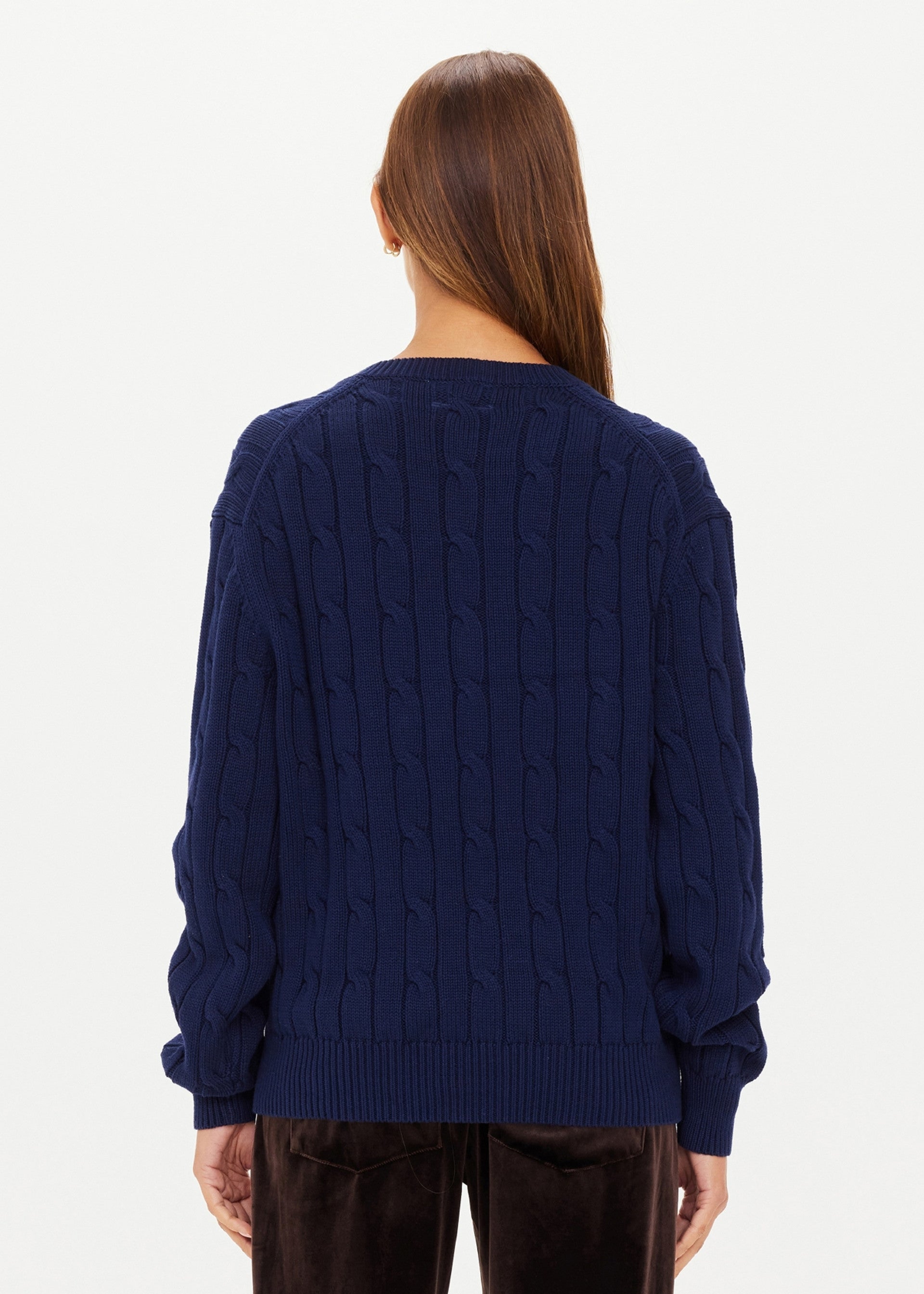 A person with long brown hair, seen from behind, wears The Upside SEYMOUR KNIT SWEATER in navy blue with dark pants against a plain white background.
