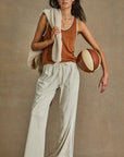 With a basketball in one hand and a beige jacket over the other shoulder, a person embodies retro basketball style in The Upside's ZAHARA JACQUIE TANK TOP, paired with light wide-legged pants, exuding effortless cool against a neutral tan background.