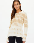 A person with long brown hair is wearing The Upside's AMANA LONG SLEEVE KNIT TOP, hand tie-dyed and made from organic cotton, paired with black leggings, standing against a plain white background.