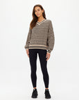 A woman with long brown hair wears The Upside CASTILLA MILLIE KNIT SWEATER, along with black leggings and sneakers. She stands against a plain white background, looking directly at the camera with a neutral expression.