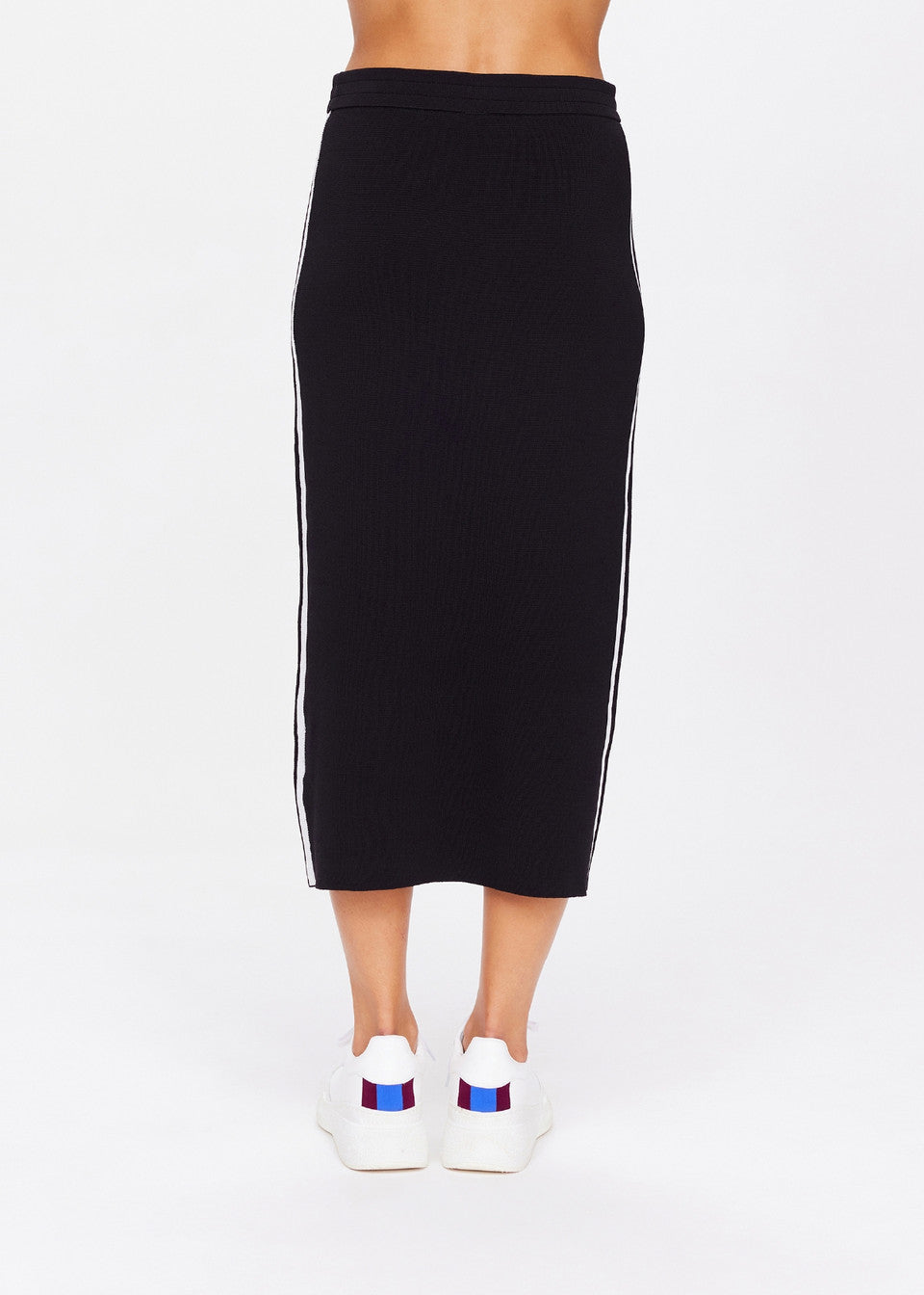 A person is wearing The Upside's ATOMIC KNIT MIDI SKIRT featuring white side stripes and an elasticated waistband, paired with white sneakers with red and blue accents, set against a plain white background.