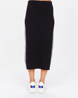 A person is wearing The Upside's ATOMIC KNIT MIDI SKIRT featuring white side stripes and an elasticated waistband, paired with white sneakers with red and blue accents, set against a plain white background.