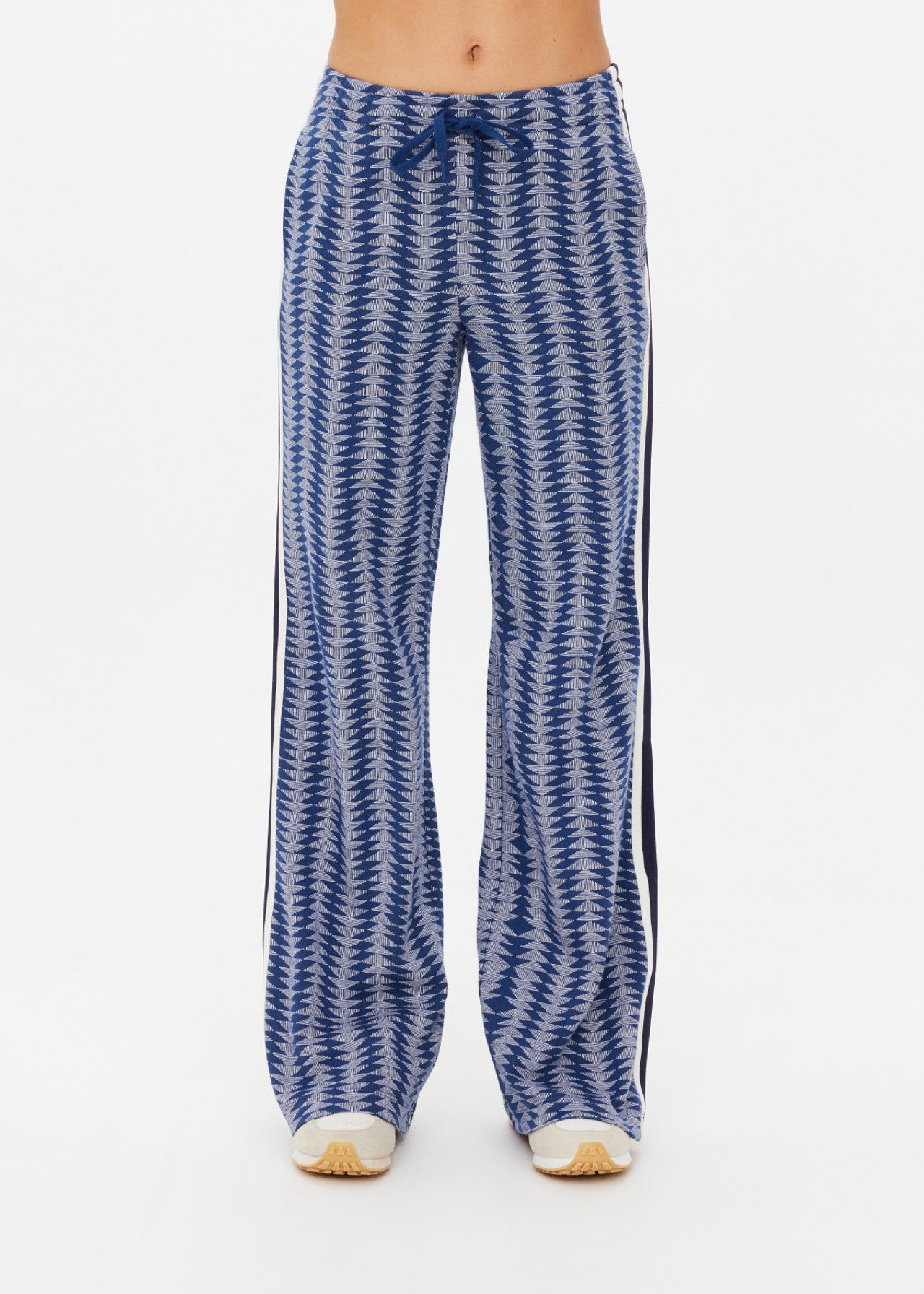 Wearing The Upside's JOIE JETSET STRAIGHT LEG PANT in geometric jacquard with a blue zigzag pattern and black side stripes, the person is shown from torso to legs. These high-waisted, wide-leg pants are made of an organic cotton blend and feature a drawstring waist against a white background.