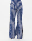 Standing against a plain white background, a person wears The Upside JOIE JETSET STRAIGHT LEG PANT, featuring a blue and white geometric jacquard pattern with sleek black vertical side stripes.