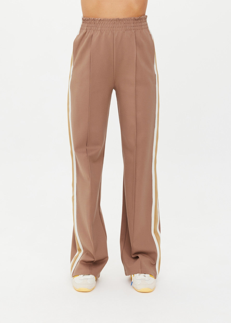 Someone wearing the stylish MONTE PANTS by The Upside, featuring high-waisted wide legs in brown with white side stripes, complemented by sleek white sneakers.