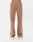 Someone wearing the stylish MONTE PANTS by The Upside, featuring high-waisted wide legs in brown with white side stripes, complemented by sleek white sneakers.