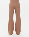 A person wearing The Upside's MONTE PANTS is shown from the back, against a white background. These high-waisted, loose-fitting pants are brown with wide legs and white side stripes, crafted from Lenzing viscose and featuring two back pockets.