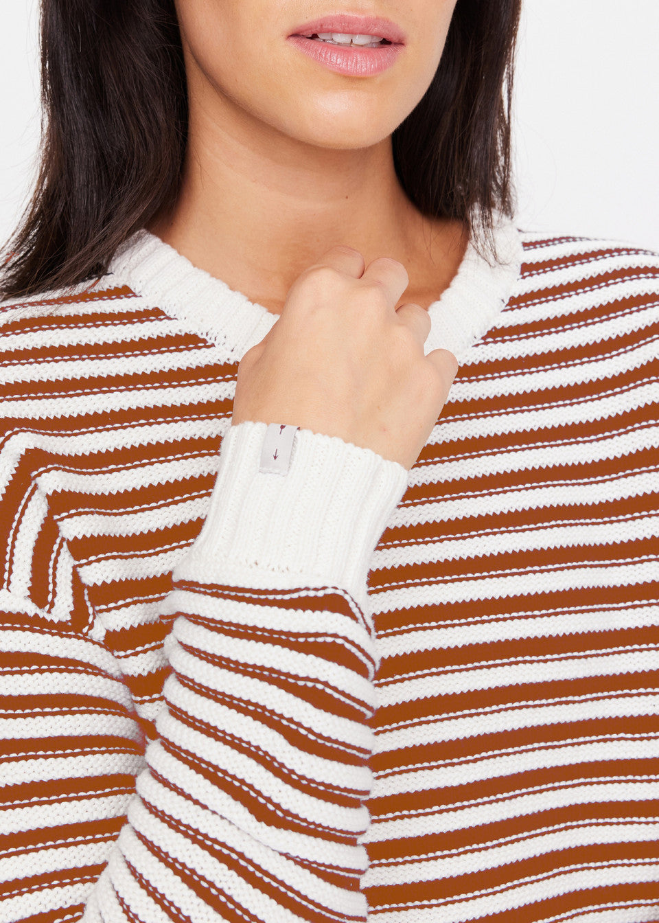 A person models The Upside's BOO KNIT JUMPER, a brown and white striped organic cotton sweater, showcasing its ribbed white cuffs and neckline while holding the collar against a plain white background.